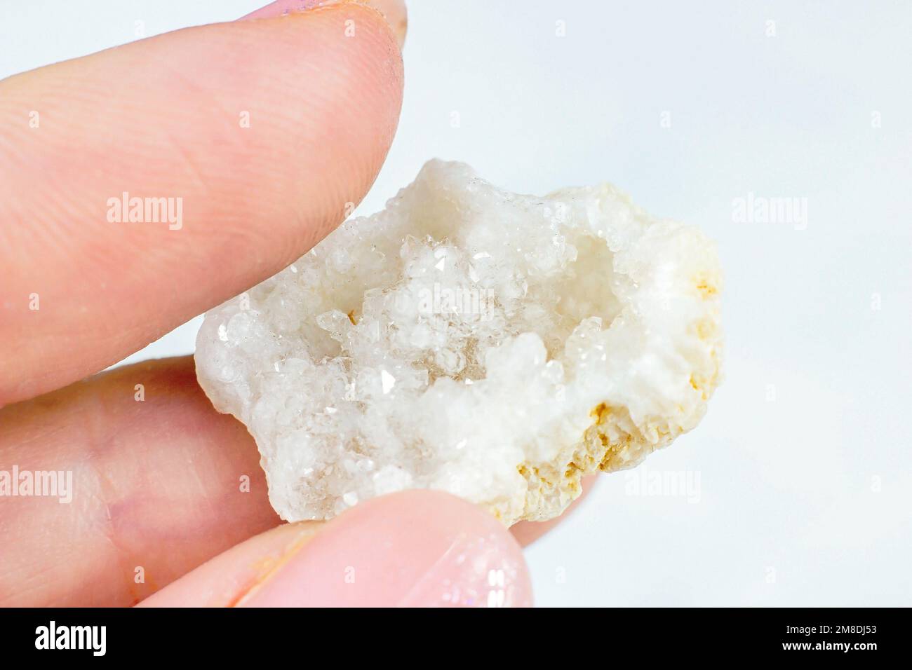 Weibliche Hand, die glänzende weiße Kristall-Agate auf hellen Hintergrund-Nahaufnahmen hält. Stockfoto