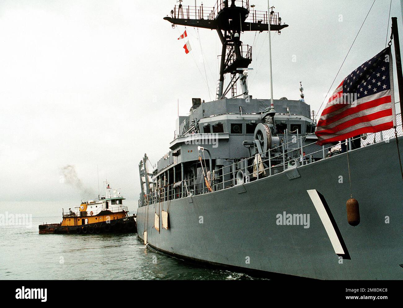Ein Schleppboot schiebt auf das Heck des Mine-Gegenmaßnahmen-Schiffs USS AVENGER (MCM-1). Der AVENGER und drei Minenräumer werden an Bord des holländischen Schwertransportschiffs SUPER SERVANT 3 zum Persischen Golf geladen, wo sie die US-Streitkräfte unterstützen werden, die als Reaktion auf die Invasion Kuwaits durch den Irak in die Region geschickt werden. Betreff Betrieb/Serie: WÜSTENSCHILD/STURMSTÜTZPUNKT: Marineflugstation, Norfolk Bundesstaat: Virginia (VA) Land: Vereinigte Staaten von Amerika (USA) Stockfoto
