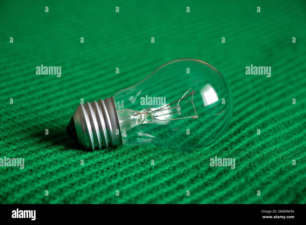 Eine Glühlampe liegt auf einem grünen Strickstoff, leicht Stockfoto