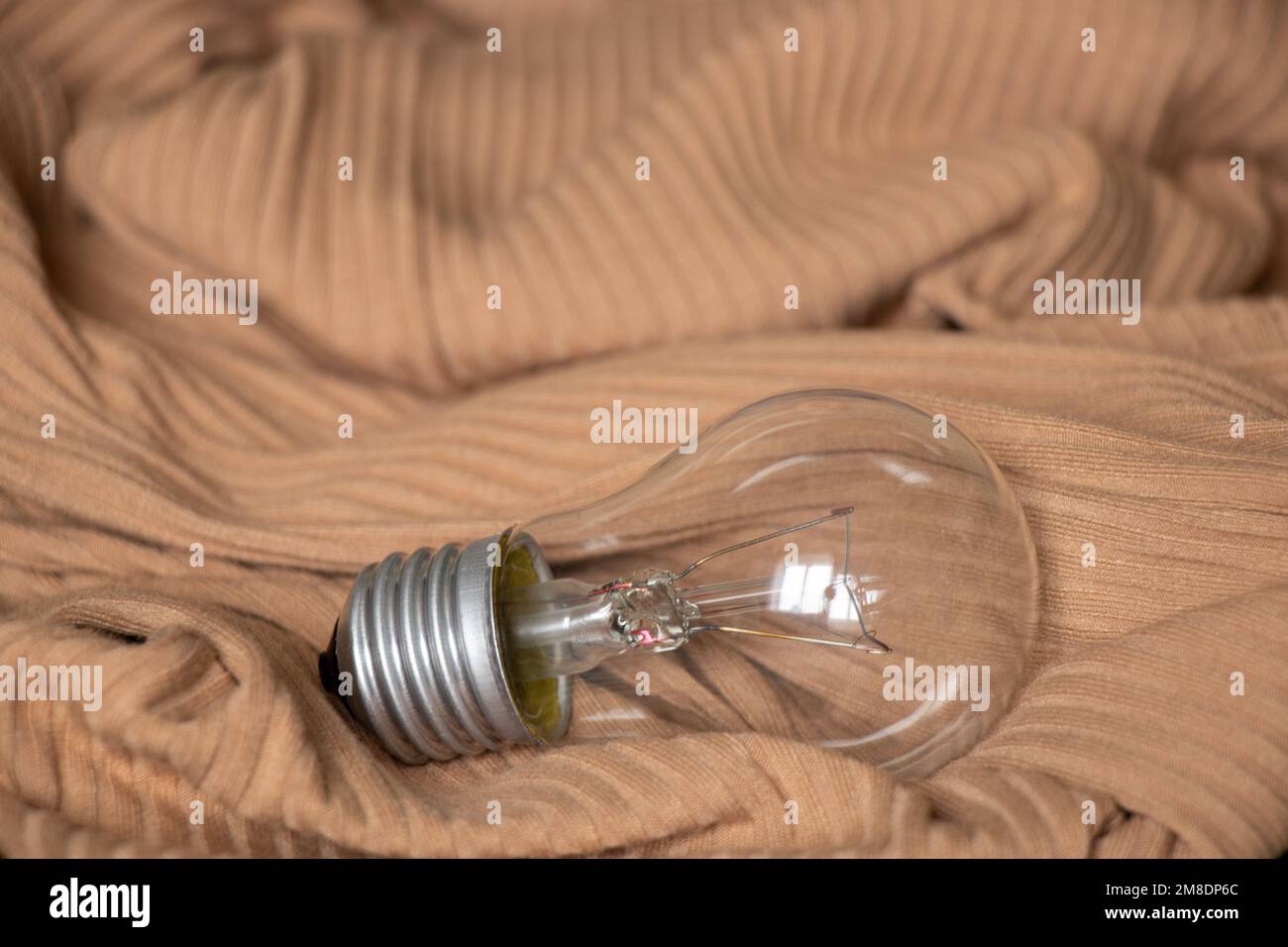 Eine Glühlampe liegt auf einem beigen, hellen Strickstoff Stockfoto