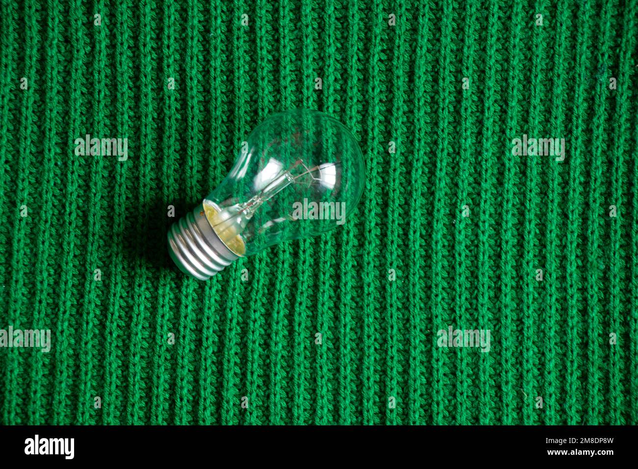 Eine Glühlampe liegt auf einem grünen Strickstoff Stockfoto