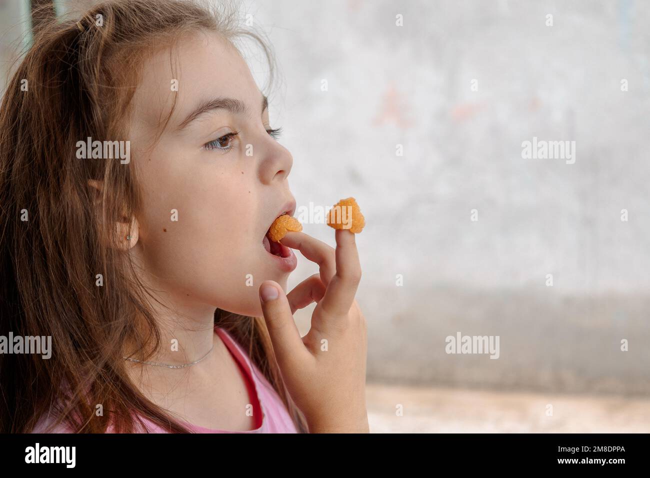 Das junge Mädchen hält gelbe Himbeeren an den Fingern und schmeckt. Hochwertige Fotos Stockfoto