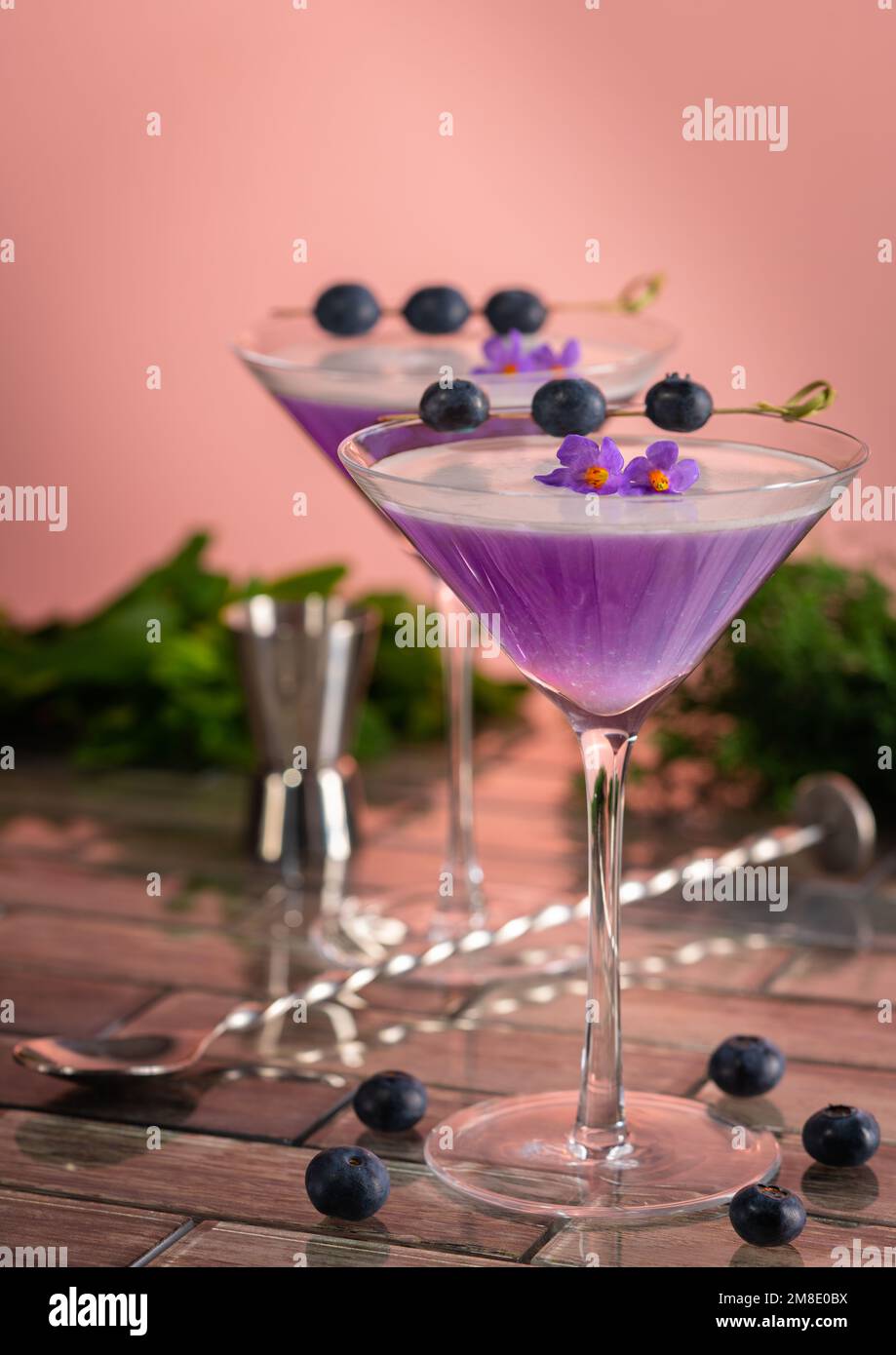 Ein Cocktail aus violettem Gin mit Schaumstoff, garniert mit Blaubeeren und Blumen, in einer Barszene. Stockfoto
