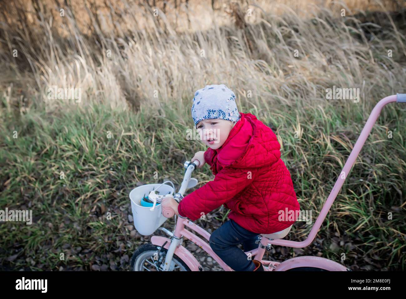 Ein kleines Mädchen auf einem Fahrrad fährt auf einer unbefestigten Straße. Ukrainischer Kindereinwanderer auf einer Spende eines gebrauchten Fahrrads durch eine Gastfamilie. Das kleine Kind lernt r Stockfoto