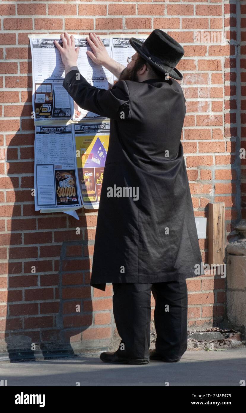 Ein chassidischer Jude hängt ein Schild mit einem Zeitplan für religiöse Ereignisse. Auf der Lee Avenue in Williamsburg, Brooklyn, New York. Stockfoto