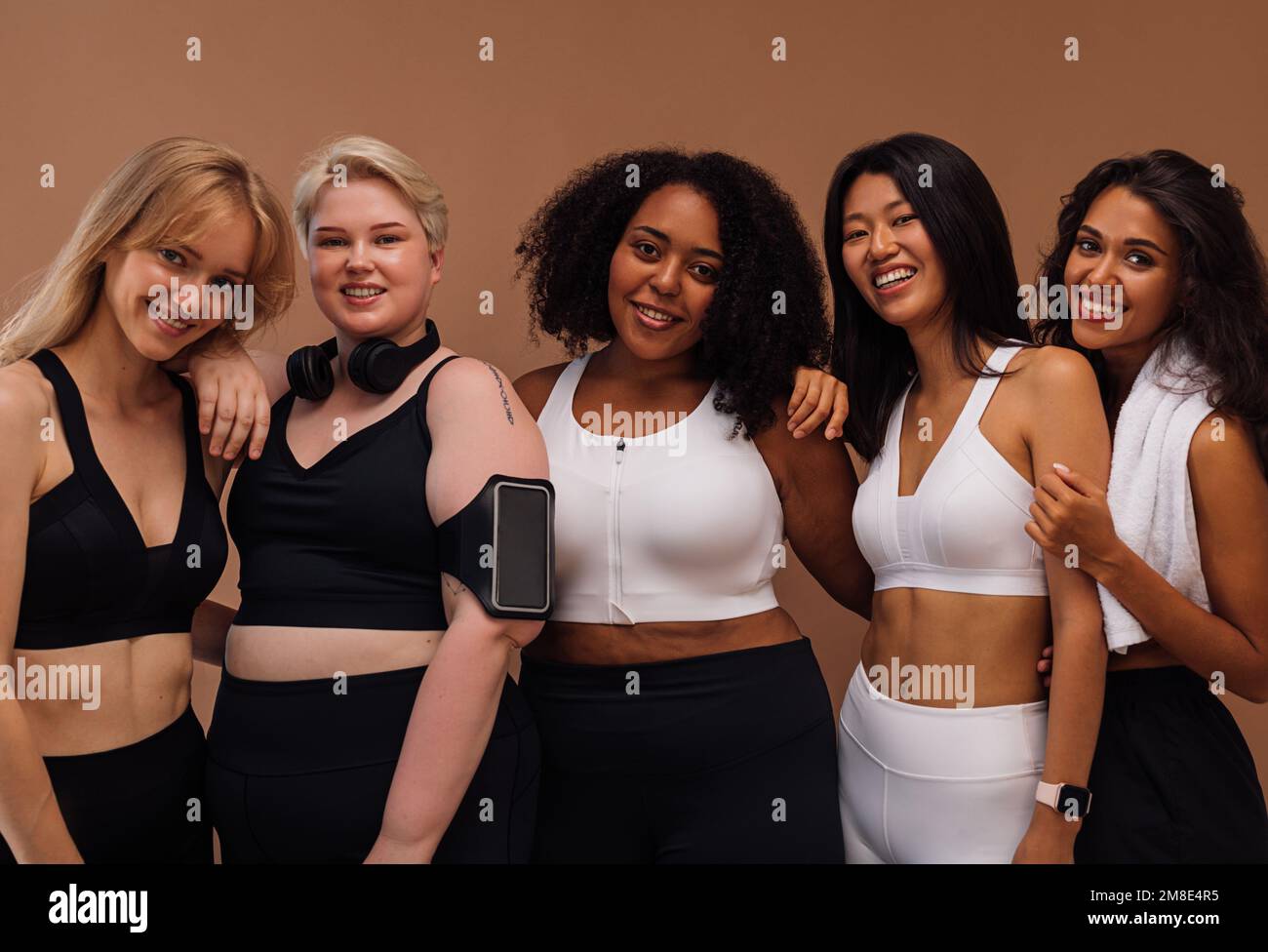 Fünf lächelnde Frauen mit verschiedenen Körpertypen und Hautfarbe, die vor braunem Hintergrund posieren Stockfoto
