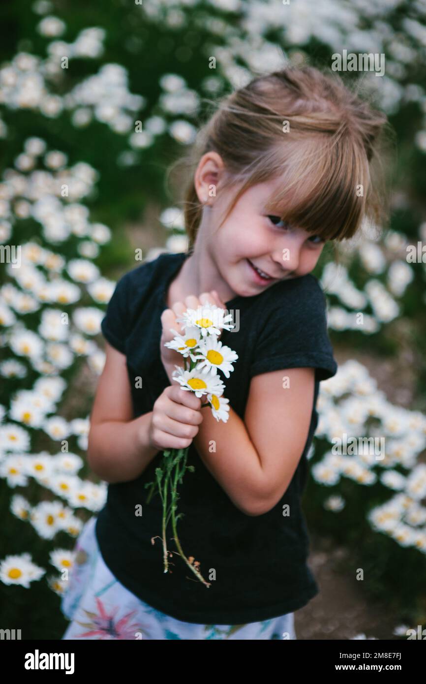 Ein Mädchen lächelt mit weißen und gelben Gänseblümchen im Blumenfeld Stockfoto