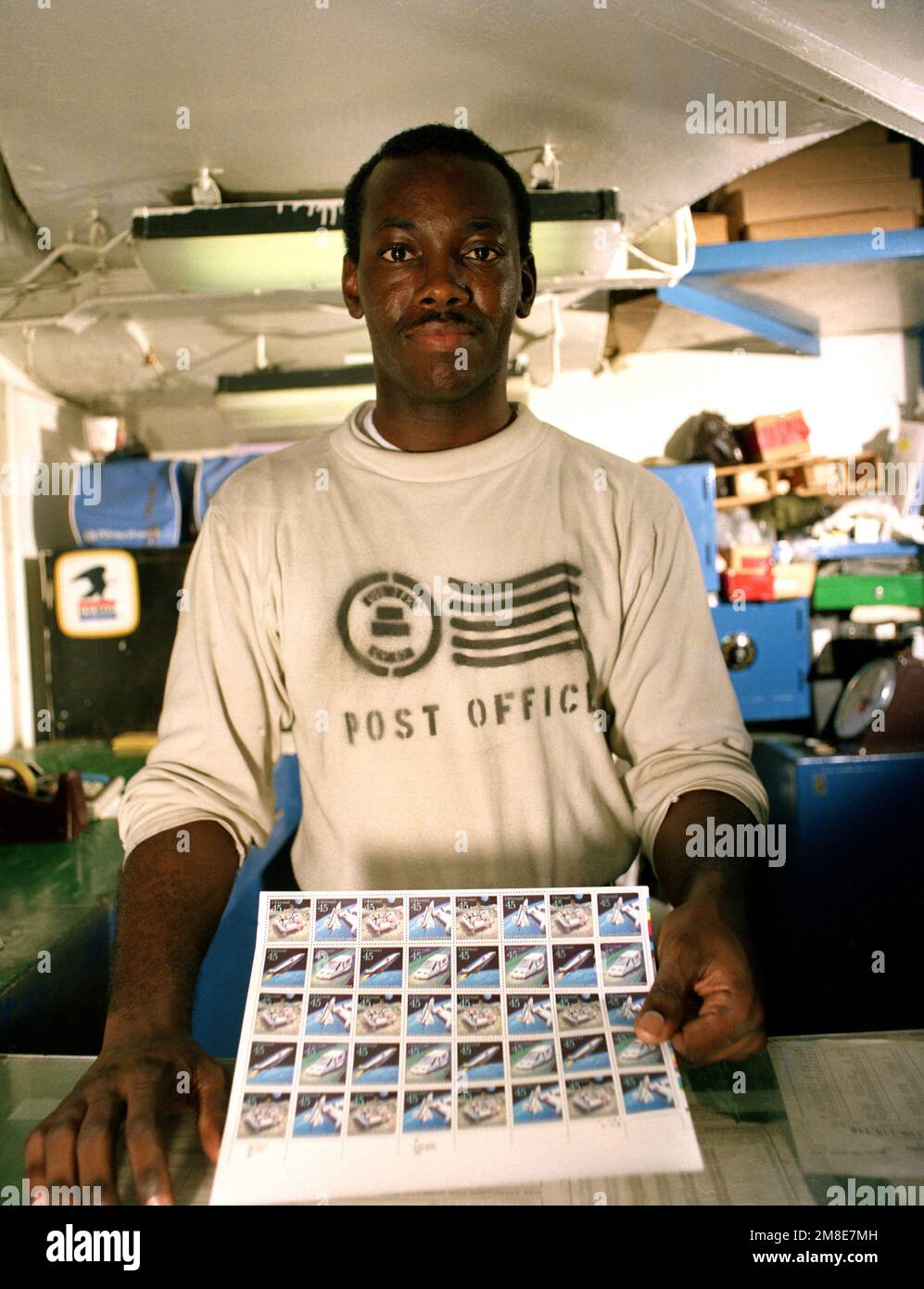 Postangestellter 2. Klasse Jerry Silas zeigt eine Seite mit Briefmarken im Postamt an Bord des Flugzeugträgers USS JOHN F. KENNEDY (CV-67). Die KENNEDY wird zur Unterstützung der Operation Desert Shield ins Rote Meer entsandt. Betreff Operation/Serie: WÜSTENSCHILDLAND: Rotes Meer Stockfoto