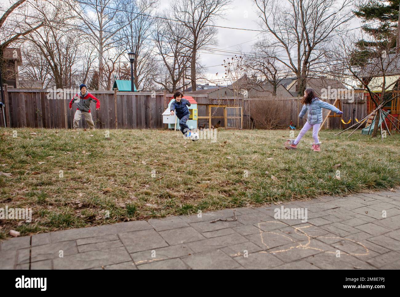 Im Winter spielt ein Junge mit seiner Familie im Vorstadtgarten Fußball Stockfoto