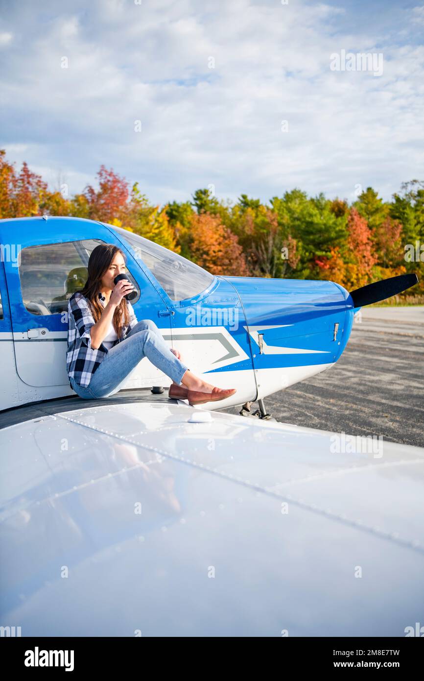 Junge BIPOC-Pilotin trinkt Morgenkaffee auf einem kleinen Flugzeugflügel Stockfoto