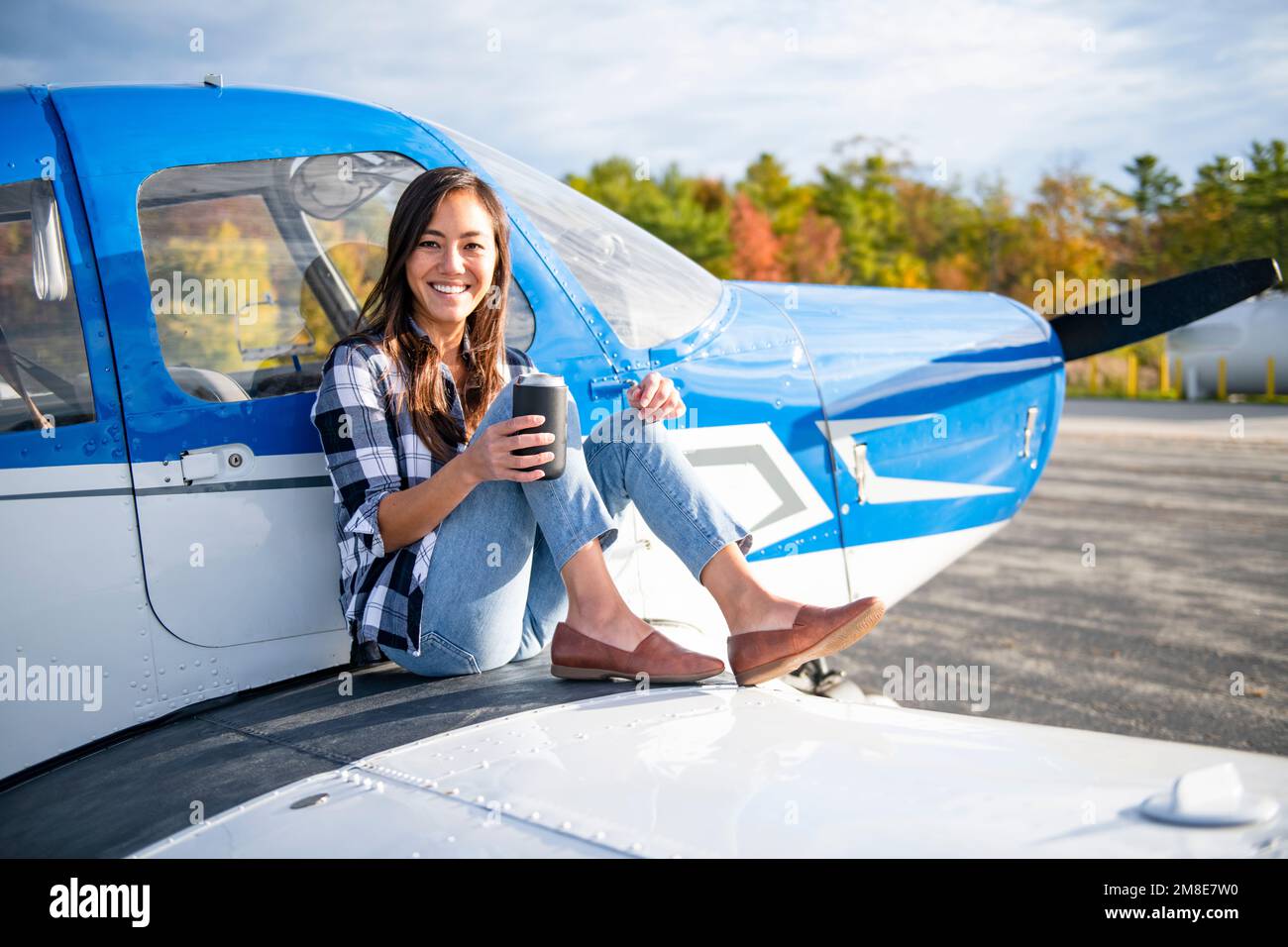 Junge BIPOC-Pilotin mit Morgenkaffee auf einem kleinen Flugzeugflügel Stockfoto