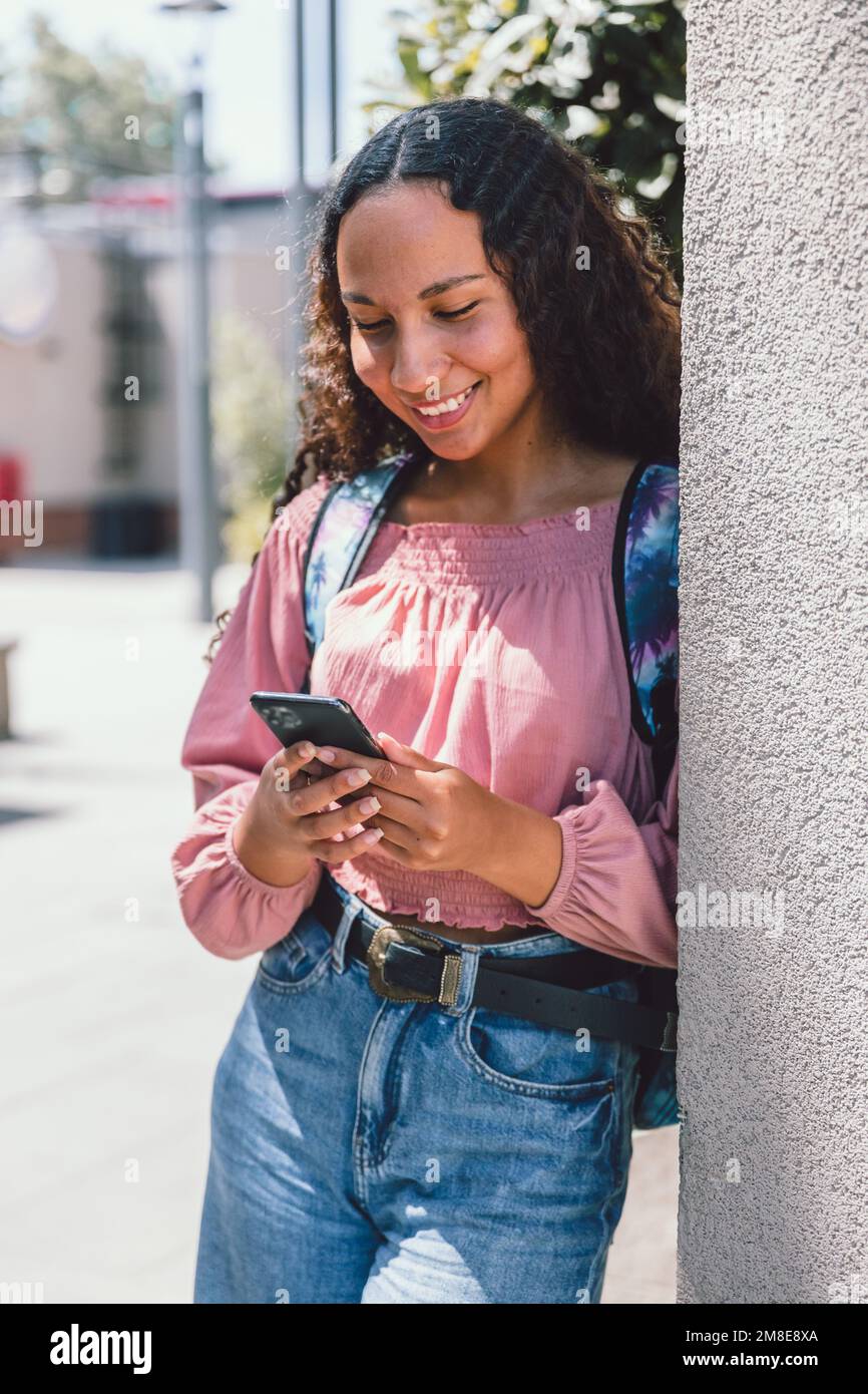 Lateinische Studentin, die lächelt und ihr Smartphone außerhalb des Campus in der Freizeit benutzt Stockfoto