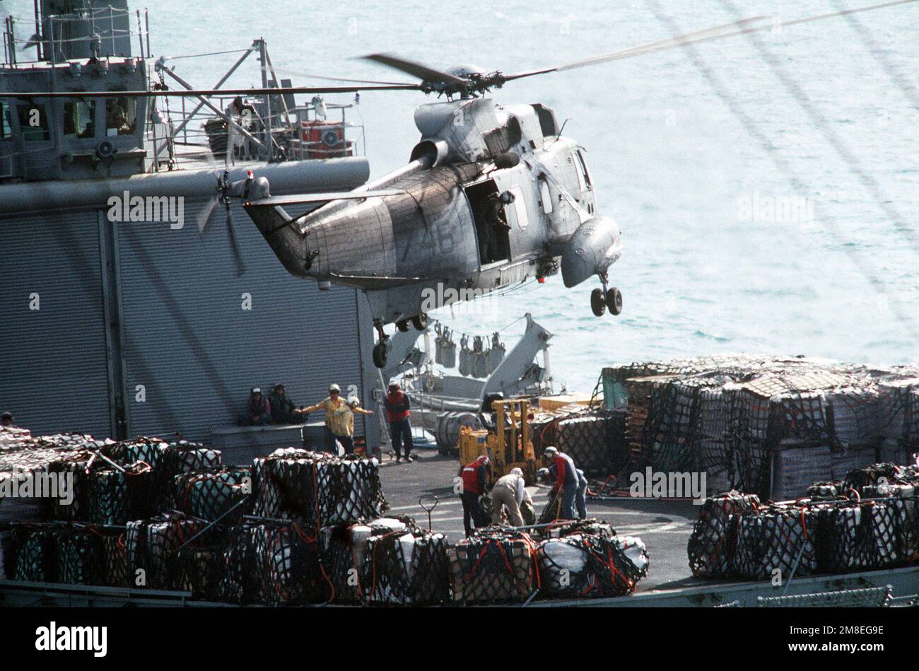 Besatzungsmitglieder an Bord des Kampfladenschiffs USS NIAGARA FALLS (AFS-3) befestigen mehrere Bündel an einer Linie, die während der Operation Desert Storm von einem SH-3H Sea King Helikopter über dem Flugdeck des Schiffs herabgesenkt wurde. Betroffene Operation/Serie: WÜSTENSTURM Land: Unbekannt Stockfoto