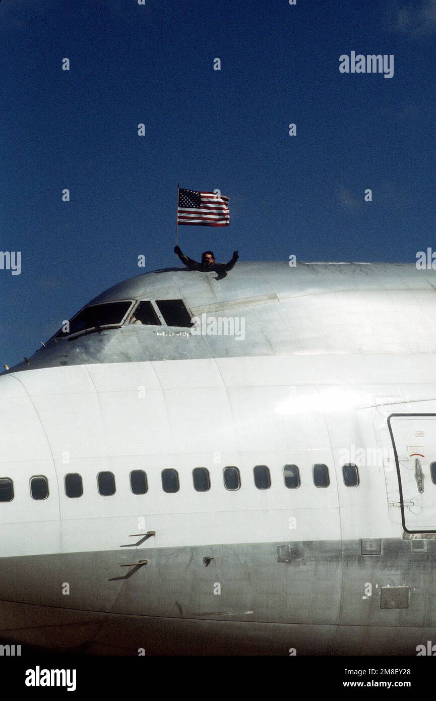 Ein Mitglied der 10. Special Forces Group (Airborne) hält eine amerikanische Flagge, während er aus der Dachluke eines Boeing 747-Flugzeugs aus dem Cockpit blickt. Der Flieger feiert die Rückkehr seiner Einheit aus dem Einsatz im Persischen Golf während der Operation Desert Storm. Betrifft Operation/Serie: WÜSTENSTURMSTÜTZPUNKT: Luftwaffenstützpunkt Westover Bundesstaat: Massachusetts (MA) Land: Vereinigte Staaten von Amerika (USA) Stockfoto