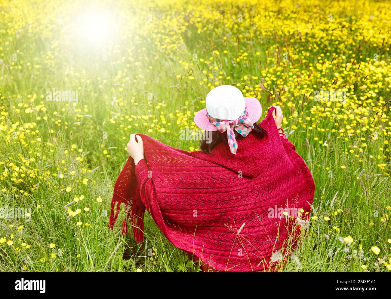 Eine Frau mitten im Feld, gefüllt mit gelben Blumen und glühendem Sonnenlicht Stockfoto