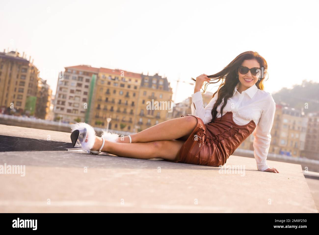 Eine Frau auf einem Urlaubsuntergang in der Stadt am Meer mit Sonnenbrille, die in die Kamera schaut Stockfoto