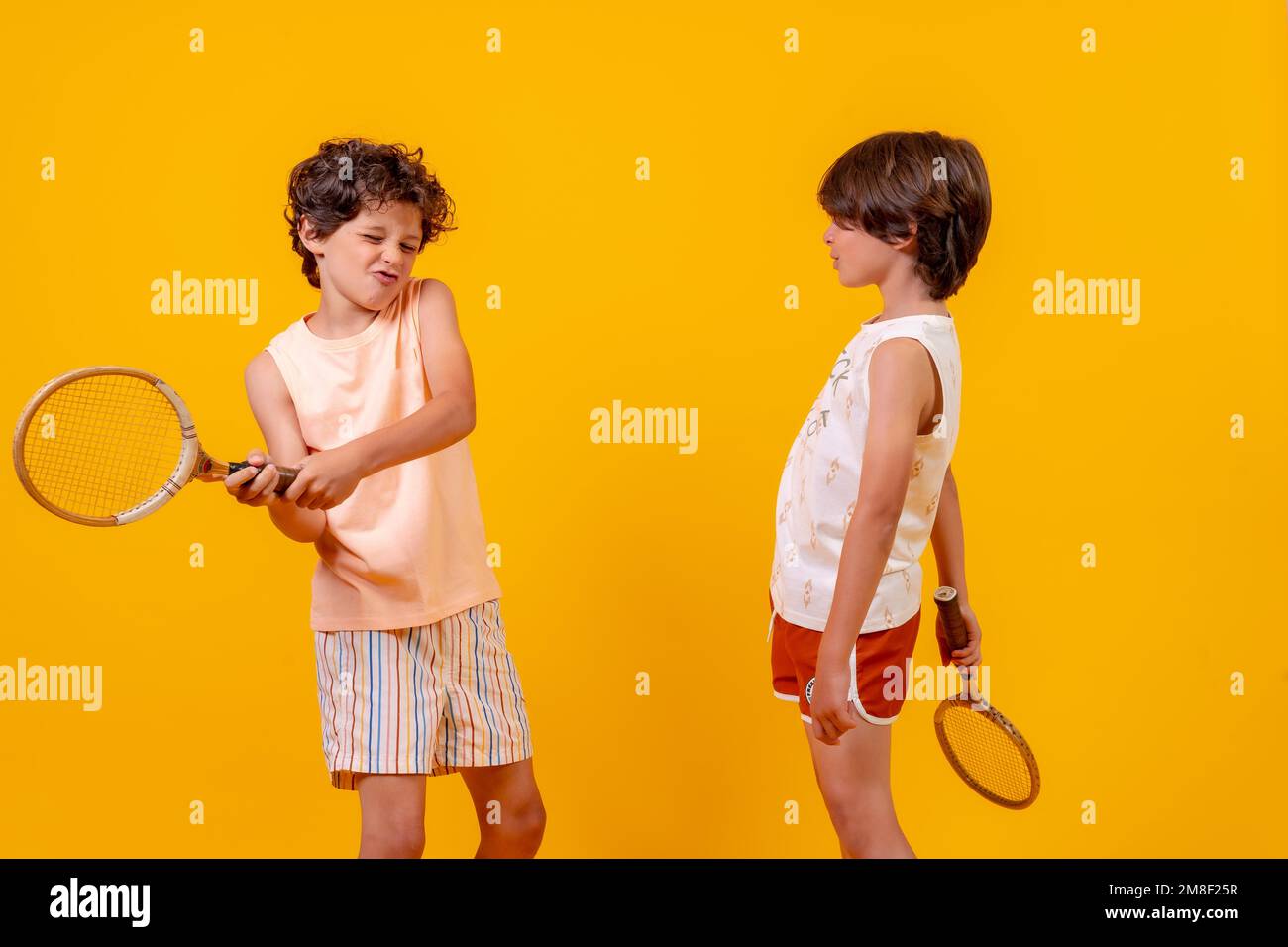 Zwei Brüder spielen Tennis und haben Spaß im Sommer, gelber Hintergrund Stockfoto