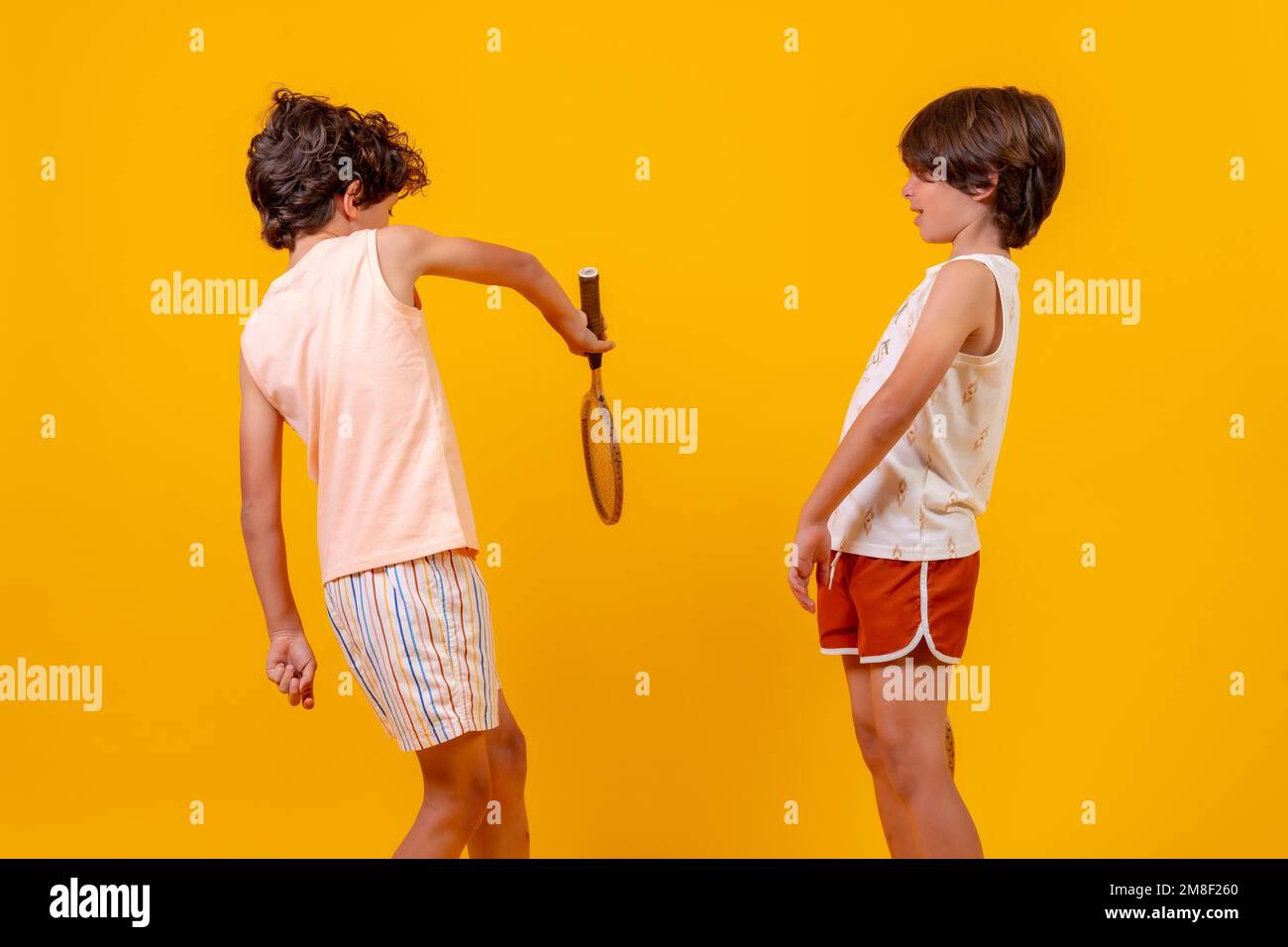 Zwei Kinder spielen Tennis und haben Spaß im Sommer, gelber Hintergrund Stockfoto
