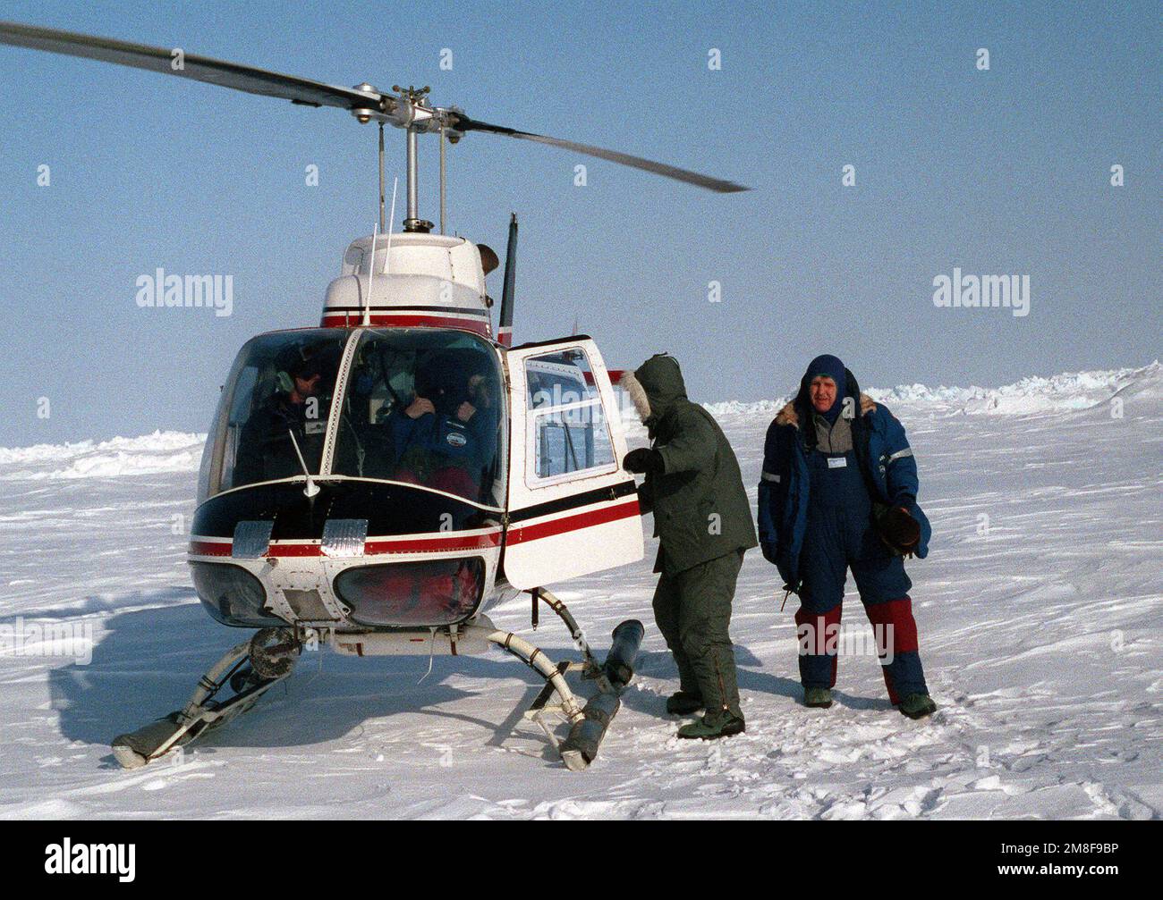 Unterstaatssekretär der Navy Daniel Howard, rechts, geht von einem gecharterten Helikopter weg, nachdem er in die Luft gegangen ist, um ein Eislager und das nuklearbetriebene Angriffs-U-Boot USS PARGO (SSN-650) nördlich des Polarkreises aus der Luft zu sehen. Howard leitet eine offizielle Party, die ins Eislager gekommen ist, um sich mit dem PARGO zu treffen. Land: Unbekannt Stockfoto