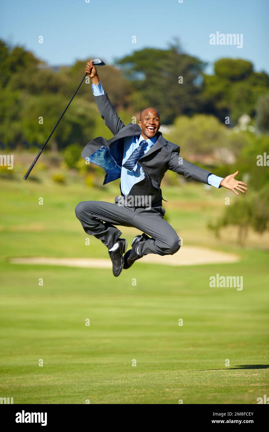 Erfolg im Geschäft UND im Sport. Ein afroamerikanischer Geschäftsmann, der freudig auf einem Golfplatz in die Luft springt. Stockfoto