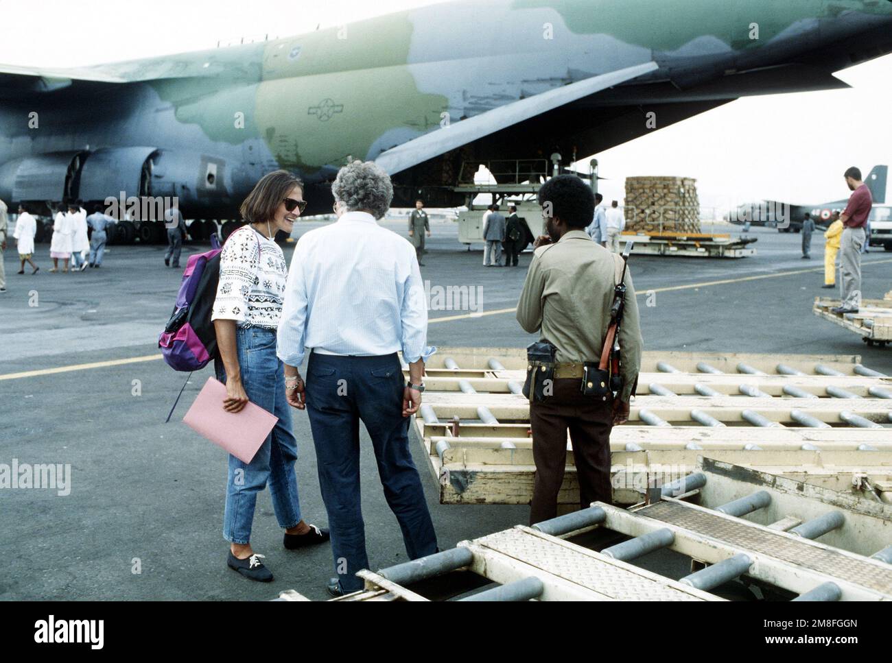 Ein Mitglied einer Rebellenfraktion, die das Gebiet kontrolliert, hört zu, wie die Arbeiter des Roten Kreuzes die Lieferung von Vorräten für die Flüchtlinge des Landes koordinieren. Meals-Ready-Eat (MREs) werden aus einem Airlift-Kommando C-5A Galaxy entladen und an Bord von Fahrzeugen des Roten Kreuzes zur Verteilung an die Opfer der Unruhen im Lande verladen. Bei den MREs handelt es sich um überschüssige militärische Vorräte, die von den Behörden des McCallum-Programms und des DOD-Programms für überschüssiges Eigentum zur Verfügung gestellt werden. Basis: Addis Abeba Land: Äthiopien (ETH) Stockfoto