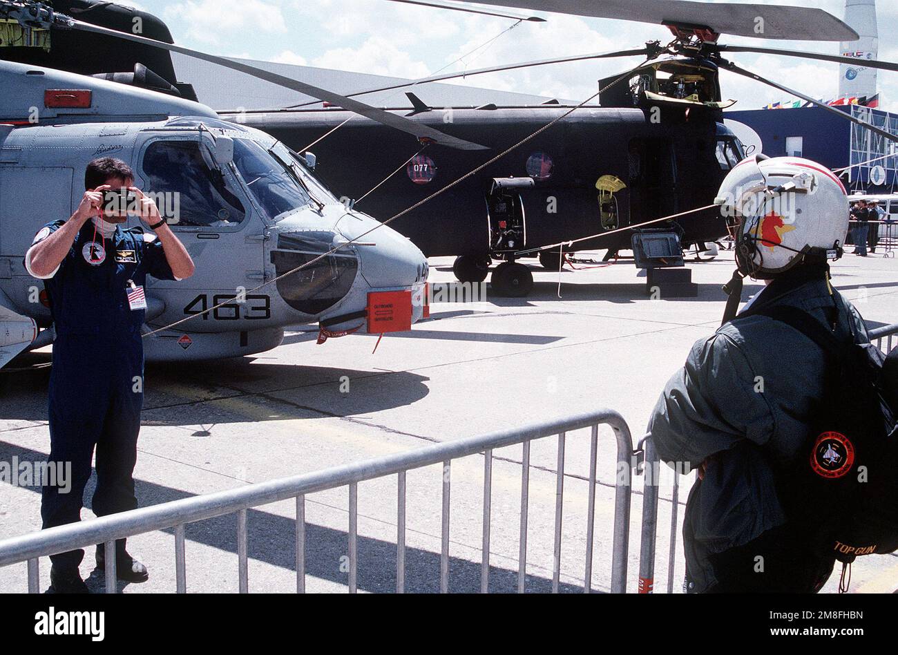 Während der Paris Air Show 1991 verwendet ein Mitglied der Light Helicopter Anti-U-Boot-Staffel 46 (HSL-46) eine Besucherkamera, um ein Foto des jungen Mannes mit seinem Flughelm zu machen. Ein SH-60B Sea Hawk Hubschrauber links und ein CH-47D Chinook Hubschrauber sind im Hintergrund. Basis: Paris Land: Frankreich (FRA) Stockfoto