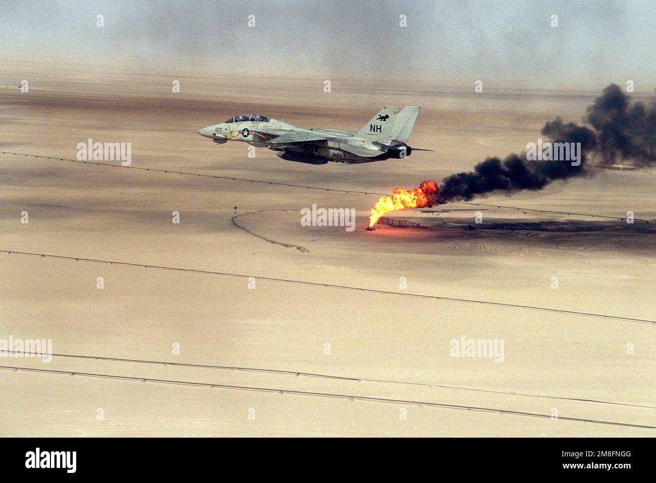 Ein Kampfgeschwader 114 (VF-114) F-14A Tomcat fliegt über einem Ölschacht, der nach Operation Desert Storm noch immer brennt. Betreff Betrieb/Serie: WÜSTENSTURMLAND: Kuwait (KWT) Stockfoto