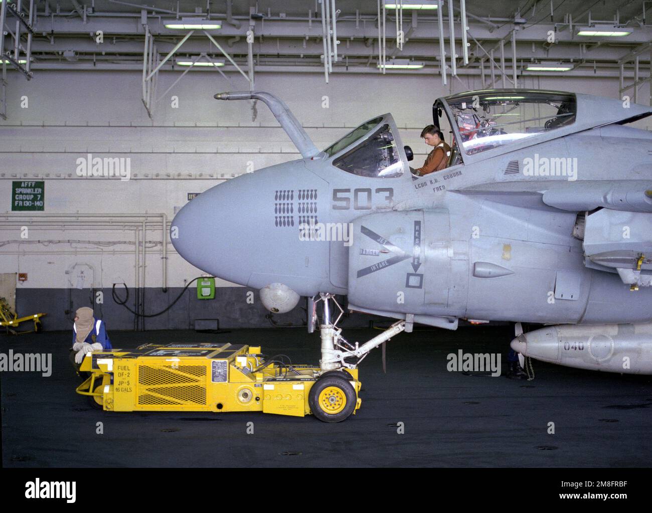 Ein Crewman, der ein SD-1D-Flugzeug besetzt, das einen Dolly beobachtet, wartet, während ein Schiffskamerad das Cockpit eines Angriffsgeschwaders 75 (VA-75) A-6E auf dem Hangardeck des Flugzeugträgers USS KITTY HAWK (CV-63) inspiziert. Land: Atlantik (AOC) Stockfoto
