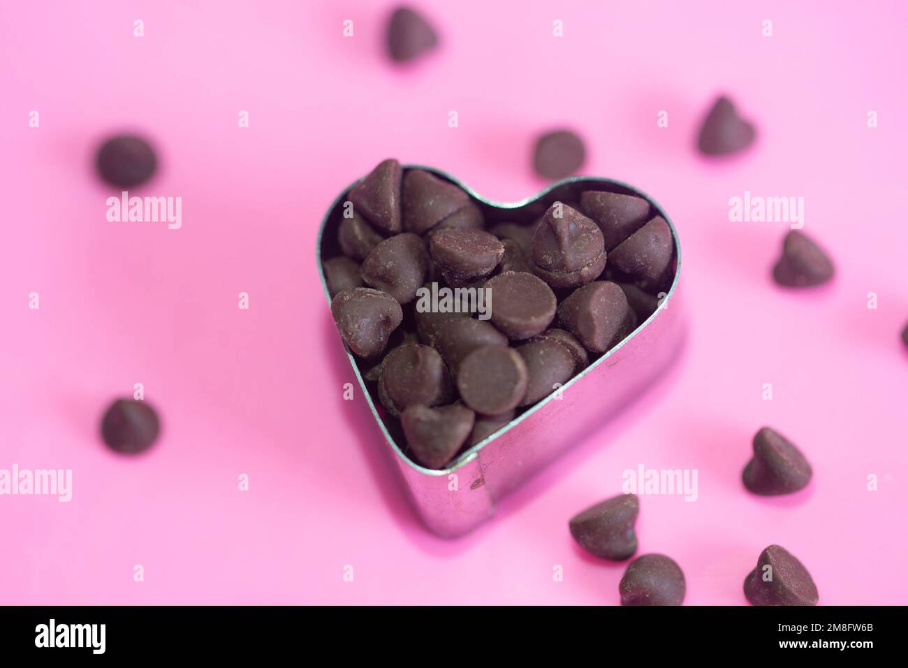 choco-Chips mit Herzschneider auf pinkfarbenem Hintergrund. Flach verlegt. Liebeskonzept. valentinstag-Konzept. Stockfoto