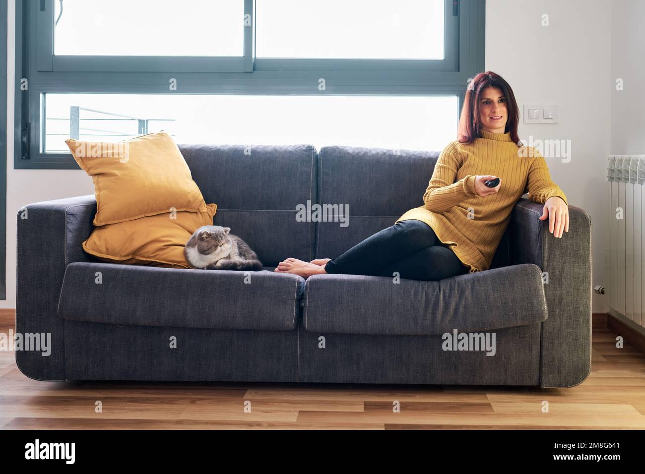Eine Frau, die Fernsehen guckt und sich dabei entspannt mit ihrer Katze auf dem Sofa sitzt. Stockfoto