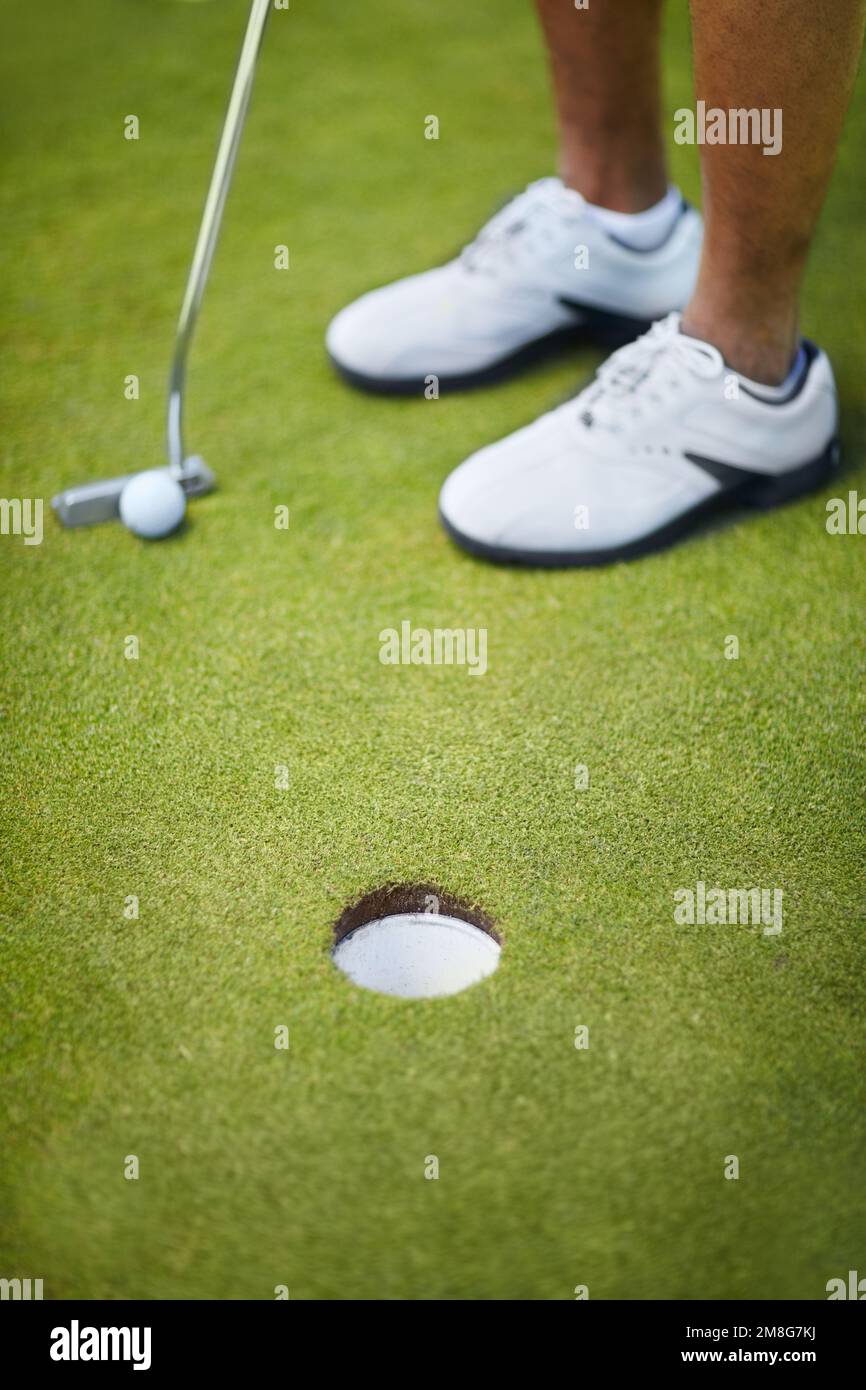 Ein einfacher Putt. Aus einem großen Winkel ausgeschnittener Schuss eines Golfers, der gerade einen Ball ins Loch wirft. Stockfoto