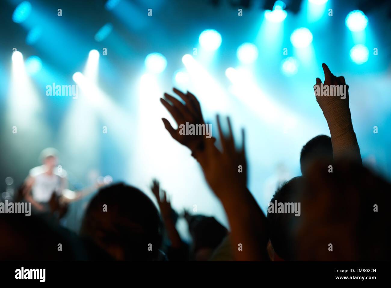 Die Nächte verschwommen. Rückblick auf ein Publikum mit erhobenen Händen bei einem Musikfestival und Lichtern, die von oben auf der Bühne nach unten strömen. Stockfoto