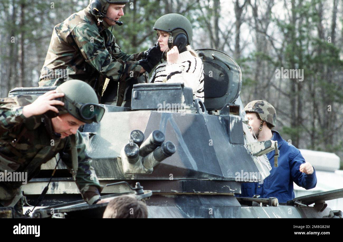 Ein Marine hilft einem Mitarbeiter des Kongresses mit ihrem Helm bei einer Vorführung der Schiffsausrüstung. Sie sind in einem leichten LAV-25-Panzerfahrzeug. Basis: Marinestützpunkt, Quantico Bundesstaat: Virginia (VA) Land: Vereinigte Staaten von Amerika (USA) Stockfoto