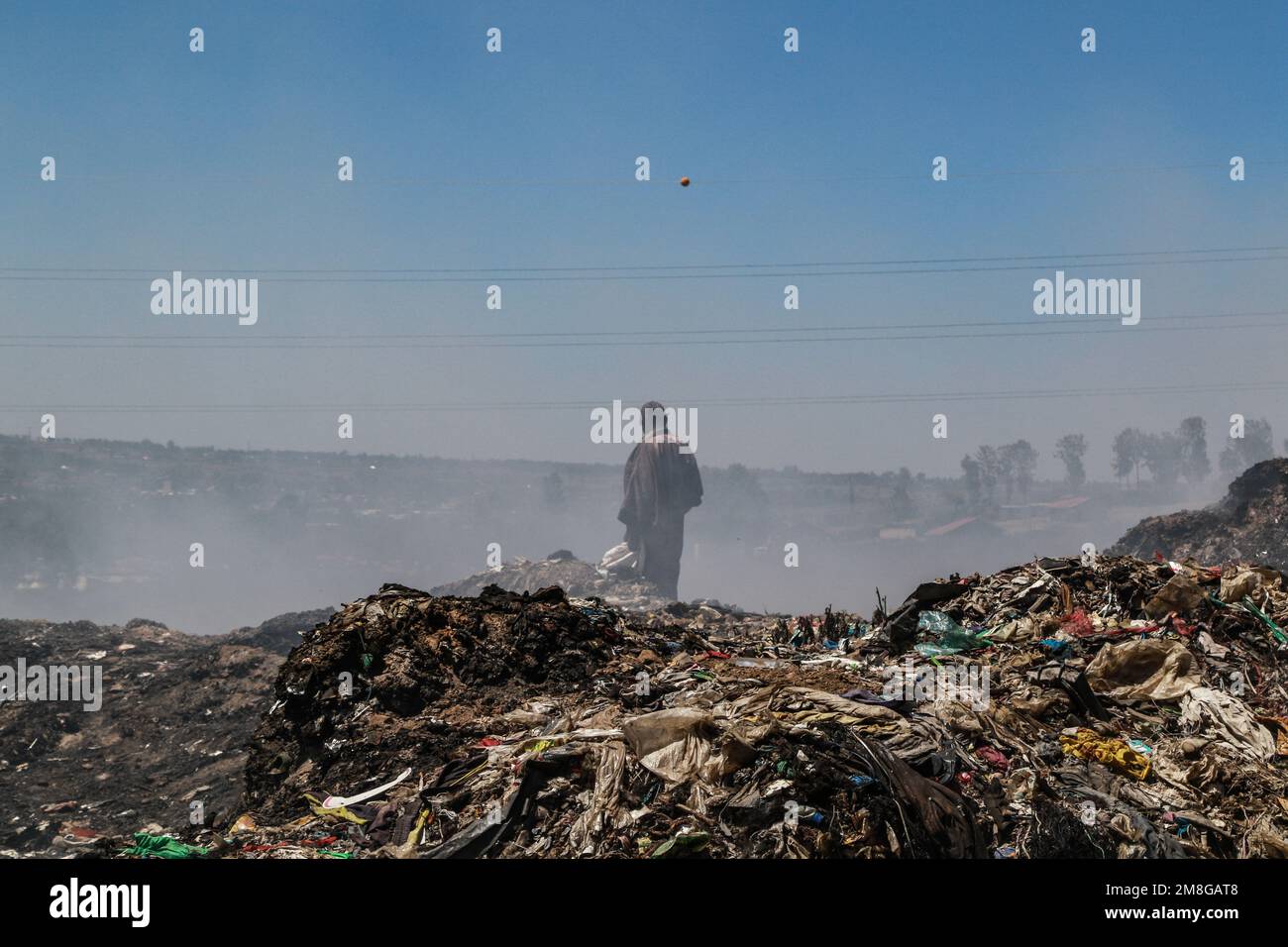 Ein Abfallsammler sammelt Abfälle, die in starkem Rauch wiederverwertet werden, indem er Müll auf dem Hauptlagerplatz von Nakuru verbrannt. Da Abfälle selten getrennt und stark mit allen Arten von Abfall vermischt werden, kann das Verbrennen potenziell giftige Dämpfe erzeugen, die ein Problem für die öffentliche Gesundheit darstellen und auch zum Klimawandel beitragen können. Gemeinden, die in der Nähe von Mülldeponien arbeiten und leben, wo Müll offen verbrannt wird, sind dem Risiko von Atemwegserkrankungen und Krebs ausgesetzt. Frauen, die diesen Dämpfen ausgesetzt sind, können unter reproduktiven Gesundheitsproblemen leiden. Stockfoto