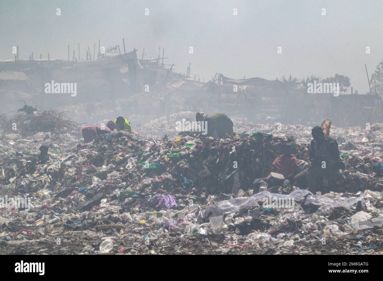 Müllsammler sammeln Abfälle, um sie in starkem Rauch zu recyceln, indem sie Müll auf dem Hauptlagerplatz von Nakuru verbrennen. Da Abfälle selten getrennt und stark mit allen Arten von Abfall vermischt werden, kann das Verbrennen potenziell giftige Dämpfe erzeugen, die ein Problem für die öffentliche Gesundheit darstellen und auch zum Klimawandel beitragen können. Gemeinden, die in der Nähe von Mülldeponien arbeiten und leben, wo Müll offen verbrannt wird, sind dem Risiko von Atemwegserkrankungen und Krebs ausgesetzt. Frauen, die diesen Dämpfen ausgesetzt sind, können unter reproduktiven Gesundheitsproblemen leiden. Stockfoto
