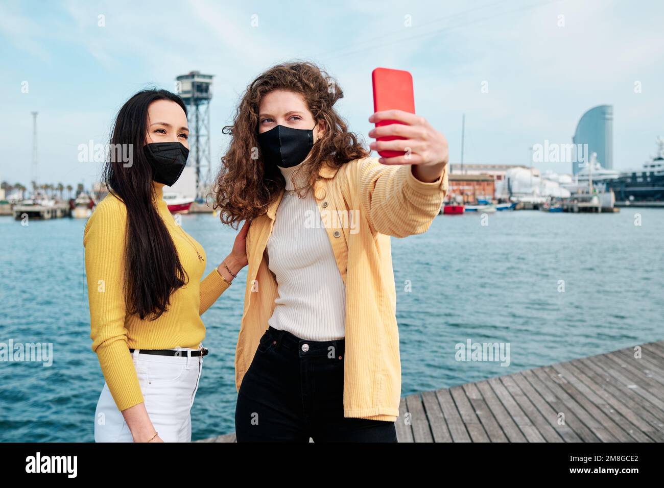 Junge Frauen mit Gesichtsmaske machen Selfies mit dem Handy im Freien. Stockfoto