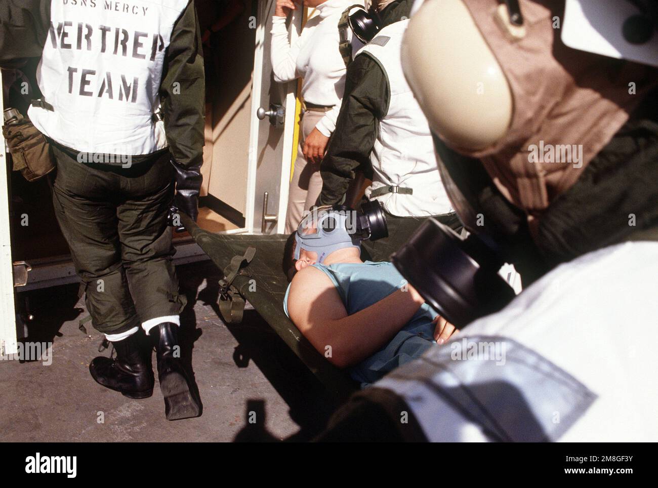 Externe Müllträger mit chemischer, biologischer und radiologischer (CBR) Kleidung und MCU-2P Gasmasken tragen einen „Patienten“ von einem Hubschrauber zu einer der Dekontaminationsstationen an Bord des Krankenhausschiffs USNS MERCY (T-AH-19) bei einer Massenübung bei Verletzten während der Operation Desert Shield. Betreff Betrieb/Serie: WÜSTENSCHILDBASIS: USNS Mercy (T-AH 19) Stockfoto