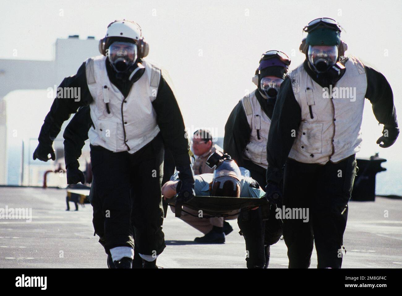 Externe Müllträger mit chemischer, biologischer und radiologischer (CBR) Kleidung und MCU-2P Gasmasken tragen einen „Patienten“ von einem Hubschrauber zu einer der Dekontaminationsstationen an Bord des Krankenhausschiffs USNS MERCY (T-AH-19) bei einer Massenübung bei Verletzten während der Operation Desert Shield. Betroffene Operation/Serie: WÜSTENSCHILD Land: Unbekannt Stockfoto