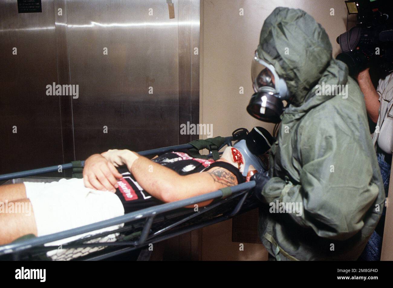 Ein Sanitäter in Schutzkleidung und eine MCU-2P-Gasmaske bereitet sich darauf vor, einen „Patienten“ während der Operation Desert Shield in einer Dekontaminationsstation während einer Massenübung an Bord des Krankenhausschiffs USNS MERCY (T-AH-19) des Sealift-Kommandos während der Operation zu spülen. Betreff Betrieb/Serie: WÜSTENSCHILDBASIS: USNS Mercy (T-AH 19) Stockfoto