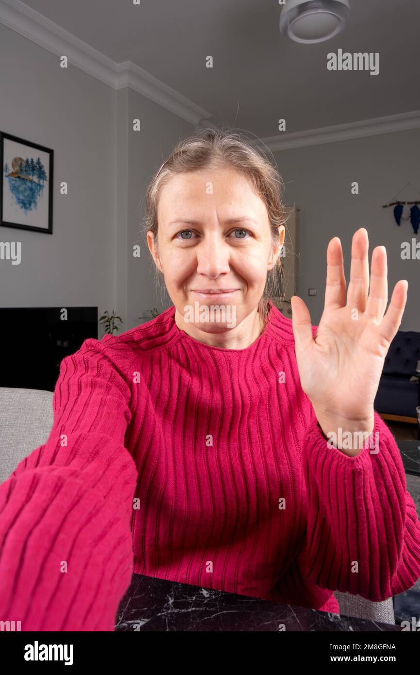 Smartphone-Kameraansicht einer Frau, die mit der Hand winkt. Telefon in der Hand halten, zu Hause sitzen, in die Kamera schauen. Ich grüße ihre Schüler, Idee eines Online-Bildungskonzepts. Stockfoto