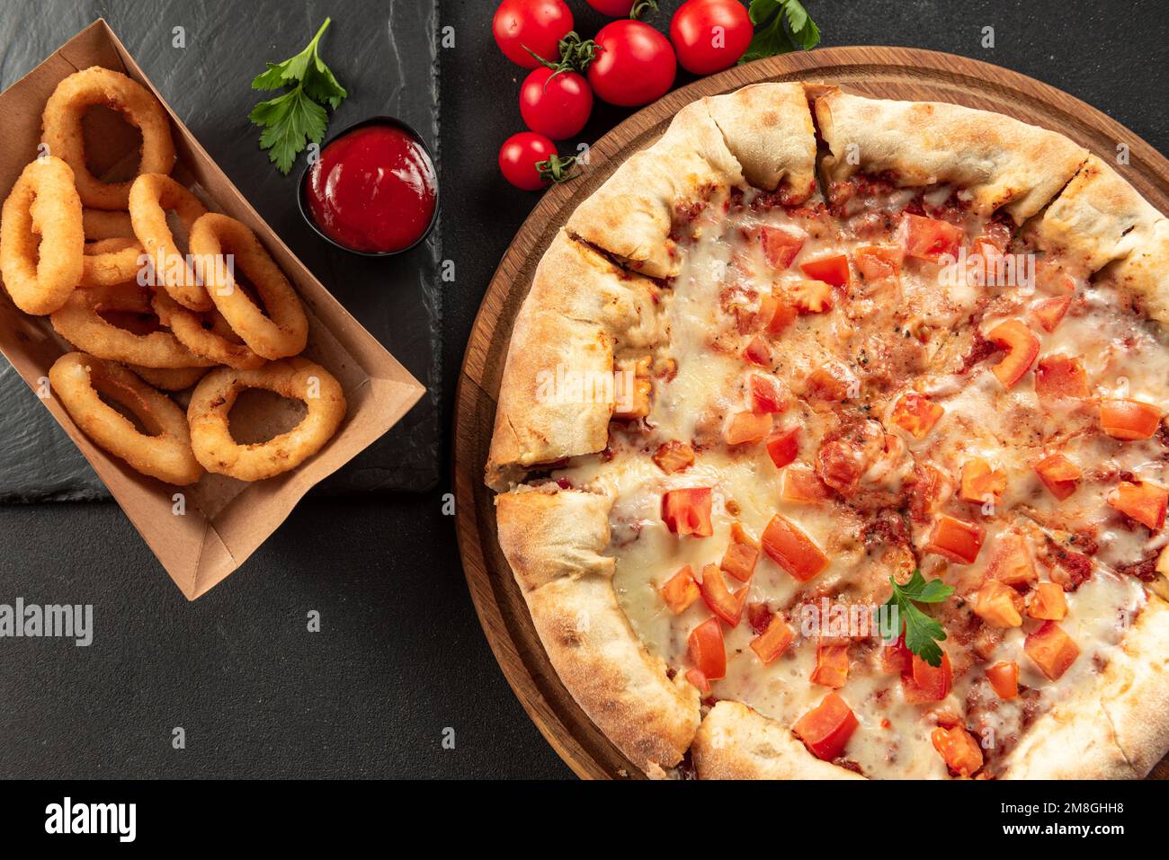 Indische Fladenbrotpizza auf dunklem Hintergrund. Indische Pizza auf dunklem Hintergrund mit Snacks. Indisches Fast Food-Set Stockfoto