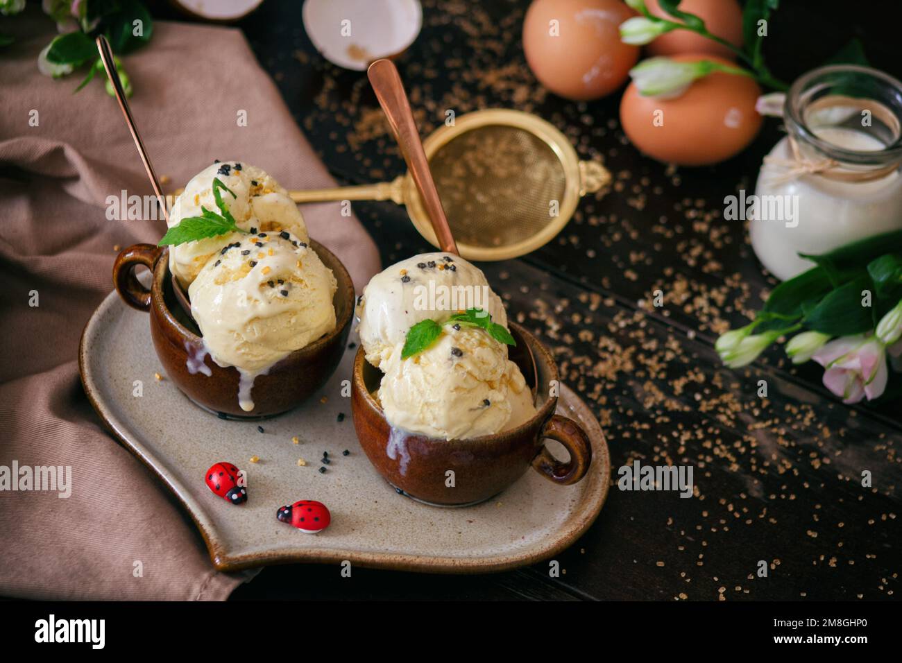 Hausgemachtes Vanilleeis auf einem Heratplate, dekoriert mit Eiern und zwei Marienkäfern. Stockfoto