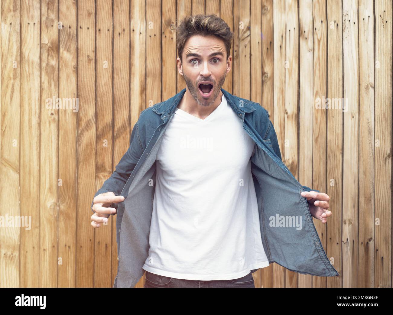 Ein junger gutaussehender Mann steht auf einem hellen Holzhintergrund. Der Kerl trägt ein weißes, leeres T-Shirt ohne Logo, was es perfekt sui macht Stockfoto