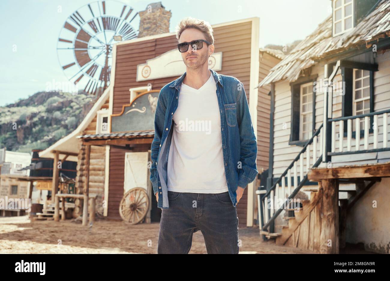 Der junge hübsche Kerl steht im Hintergrund einer westlichen Stadt. Der Mann trägt ein weißes, leeres T-Shirt ohne Logo. Vertikales Modell. Stockfoto