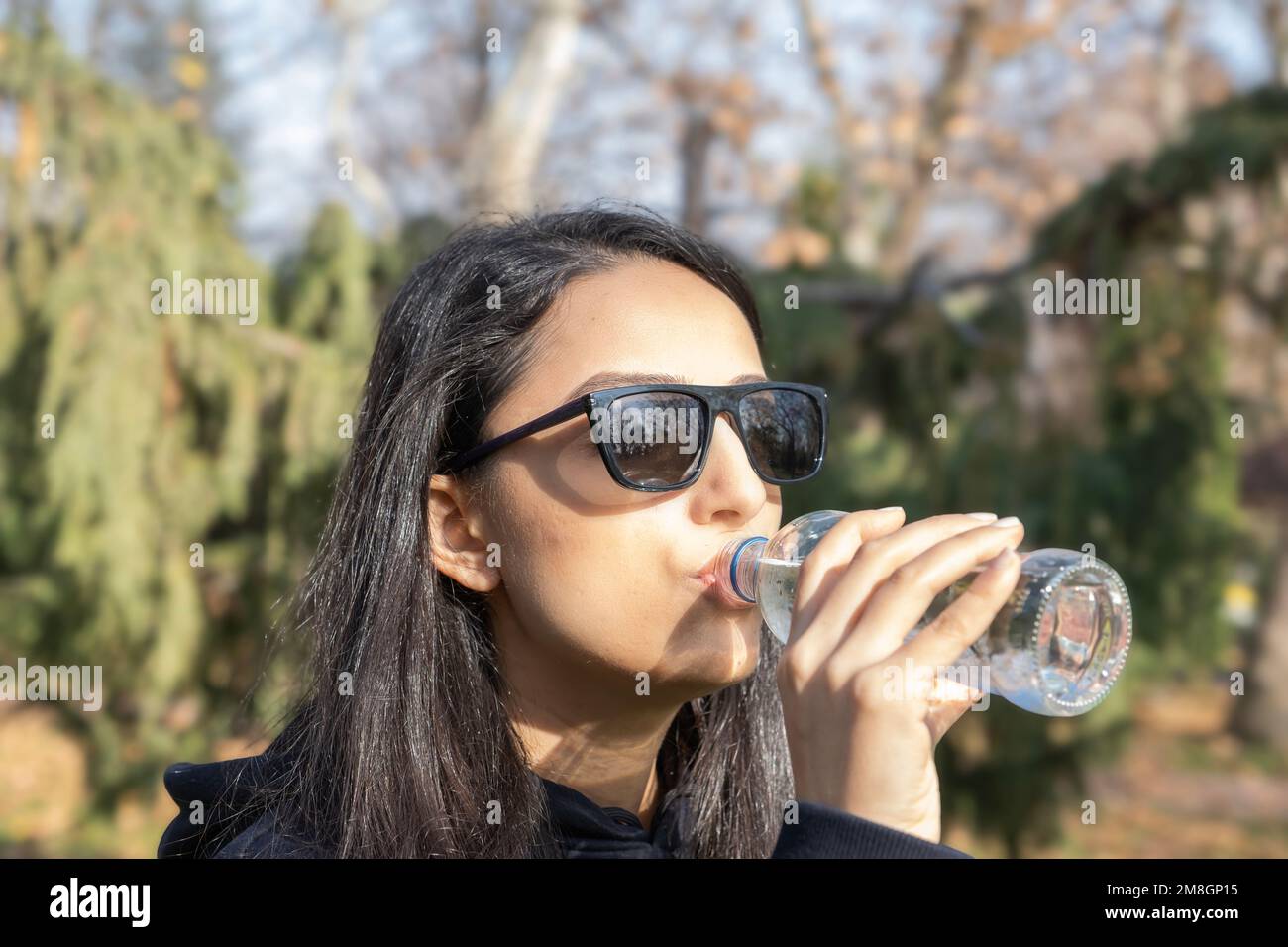 Eine Frau, die draußen Wasser trinkt. Mit Glasflasche. Positiv durstiges Millennialmädchen, das reines stilles Aqua trinkt. Wandern am sonnigen Herbsttag. Stockfoto