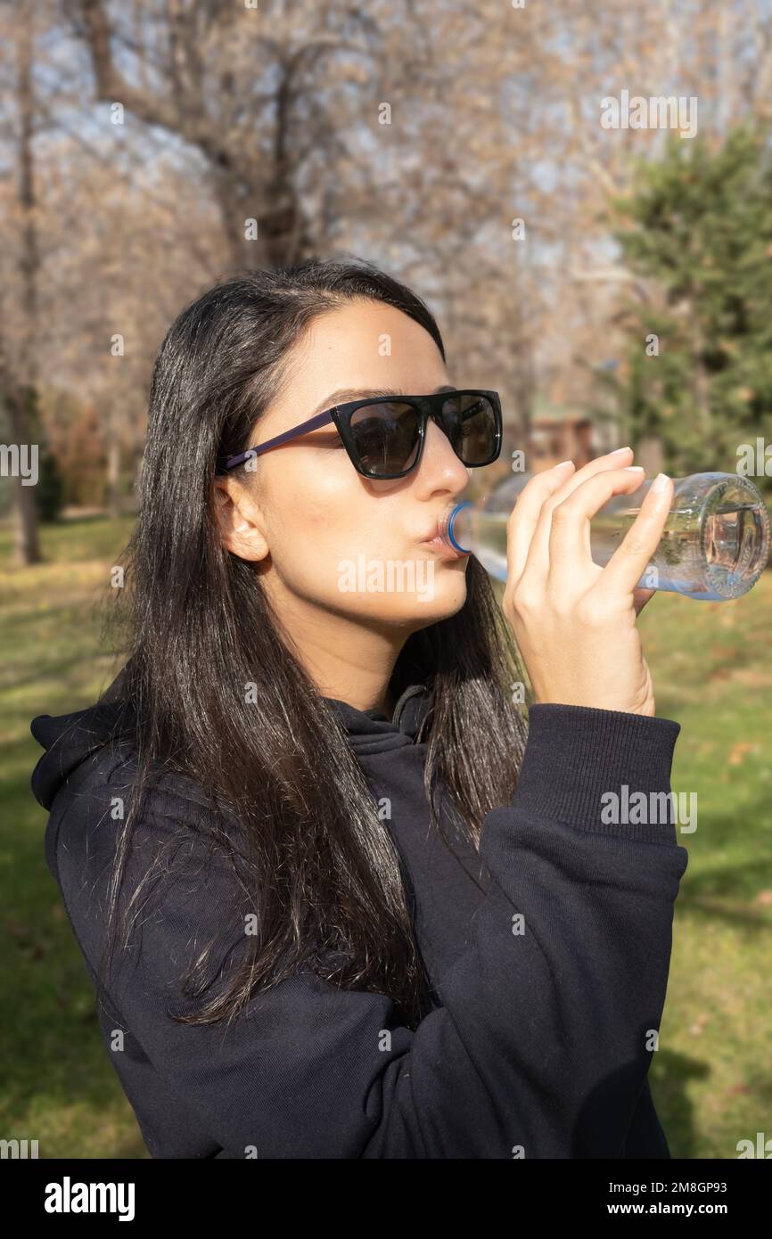 Vertikales Bild einer weissen Frau, die Wasser aus der Flasche trinkt. Draußen, sonniger Herbsttag. Durstige Frau, gesunder Lebensstil, Kopierraum. Stockfoto