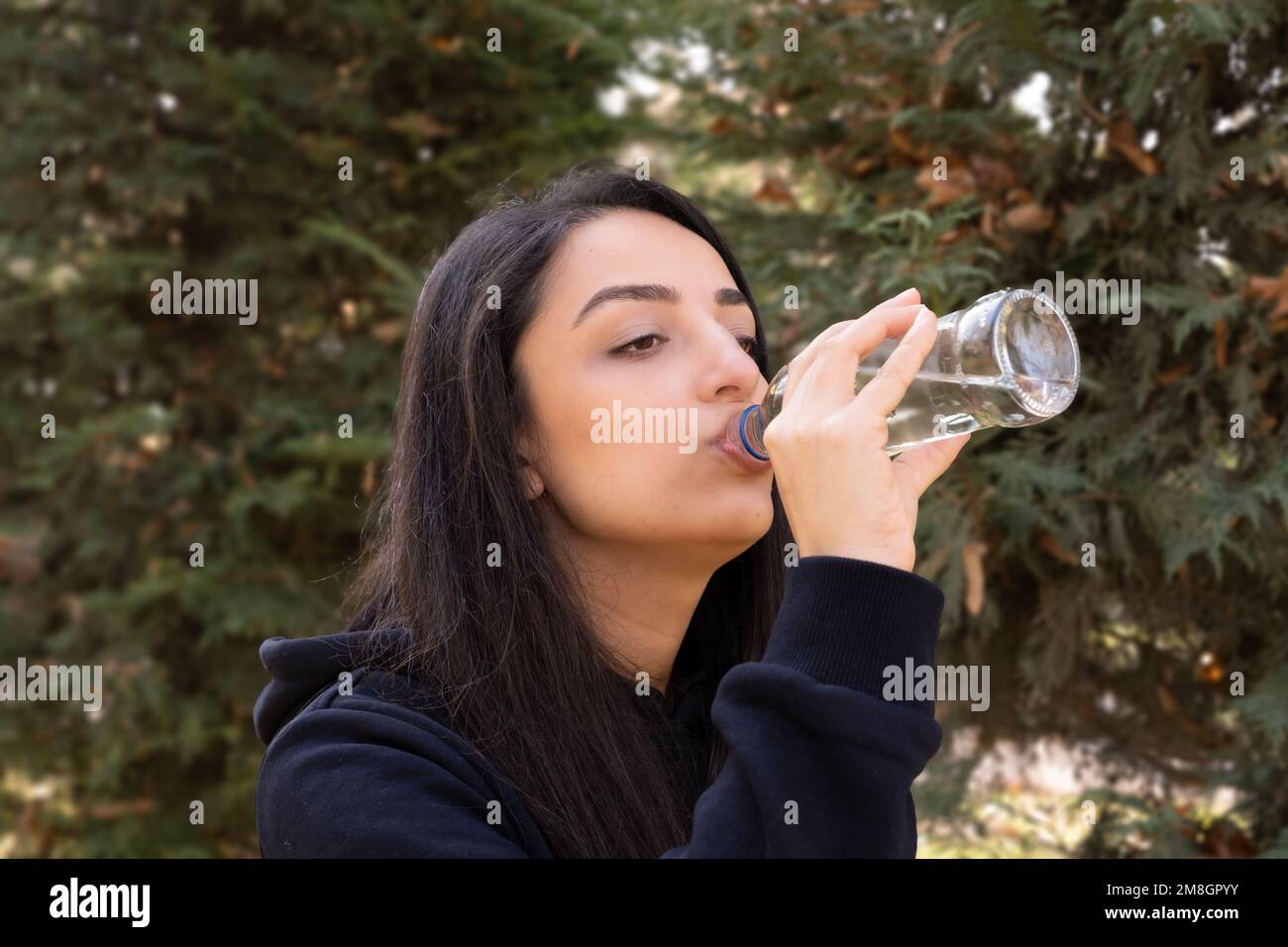 Seitenansicht des Trinkwassers einer weissen Frau. Genießen Sie reines, frisches Mineralwasser. Durstiges Mädchen nach einem Spaziergang oder Joggen im Freien. Stockfoto