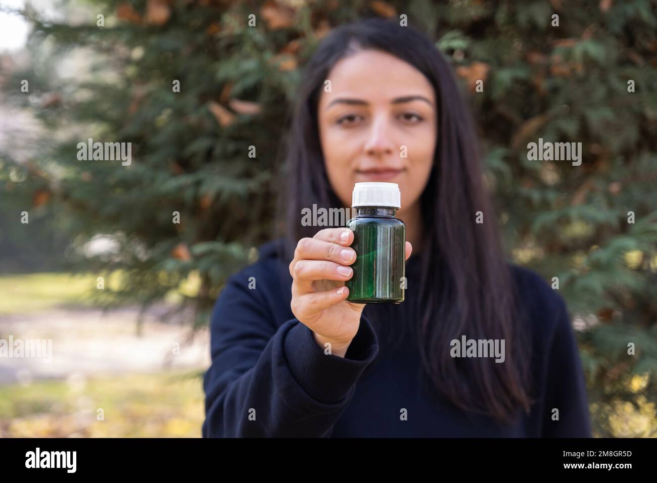 Eine Frau, die eine Flasche mit grünen Glaspillen hält. Vitamin, Medizin, Behandlungskonzept. Empfehlung eines gesunden Lebensstils. Im Herbst im Park. Stockfoto