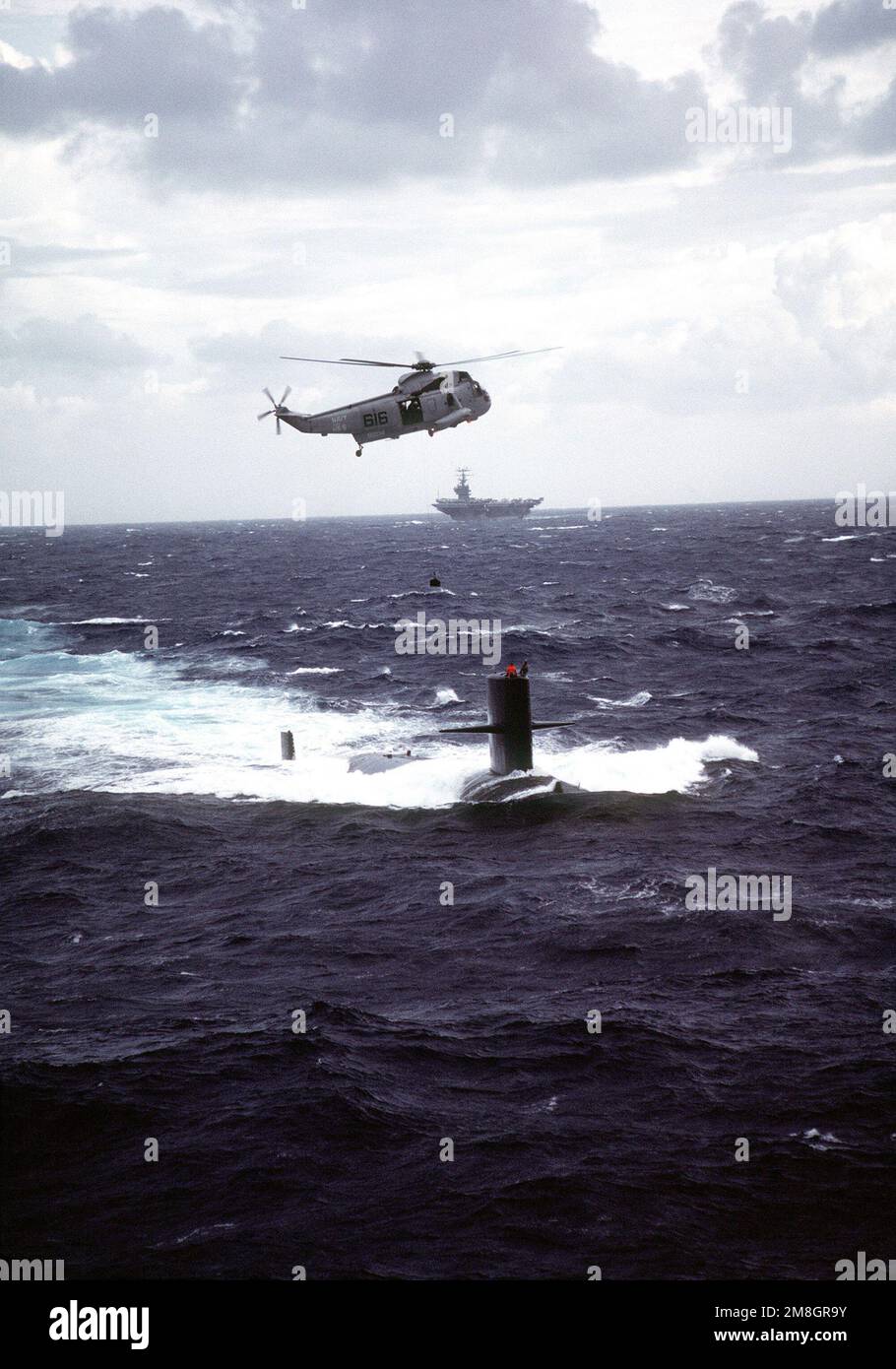 Ein Hubschrauber-U-Boot-Abwehrstaffel (HS-5) SH-3 Sea King Hubschrauber schwebt über dem nuklearbetriebenen Angriffs-U-Boot USS HAMMERHEAD (SSN-663), während er sich darauf vorbereitet, ein Geschenk des kommandierenden Offiziers des nuklearbetriebenen Flugzeugträgers GEORGE WASHINGTON (CVN-73), Hintergrund, an die Crew des HAMMERHEADS zu übergeben. Land: Atlantik (AOC) Stockfoto