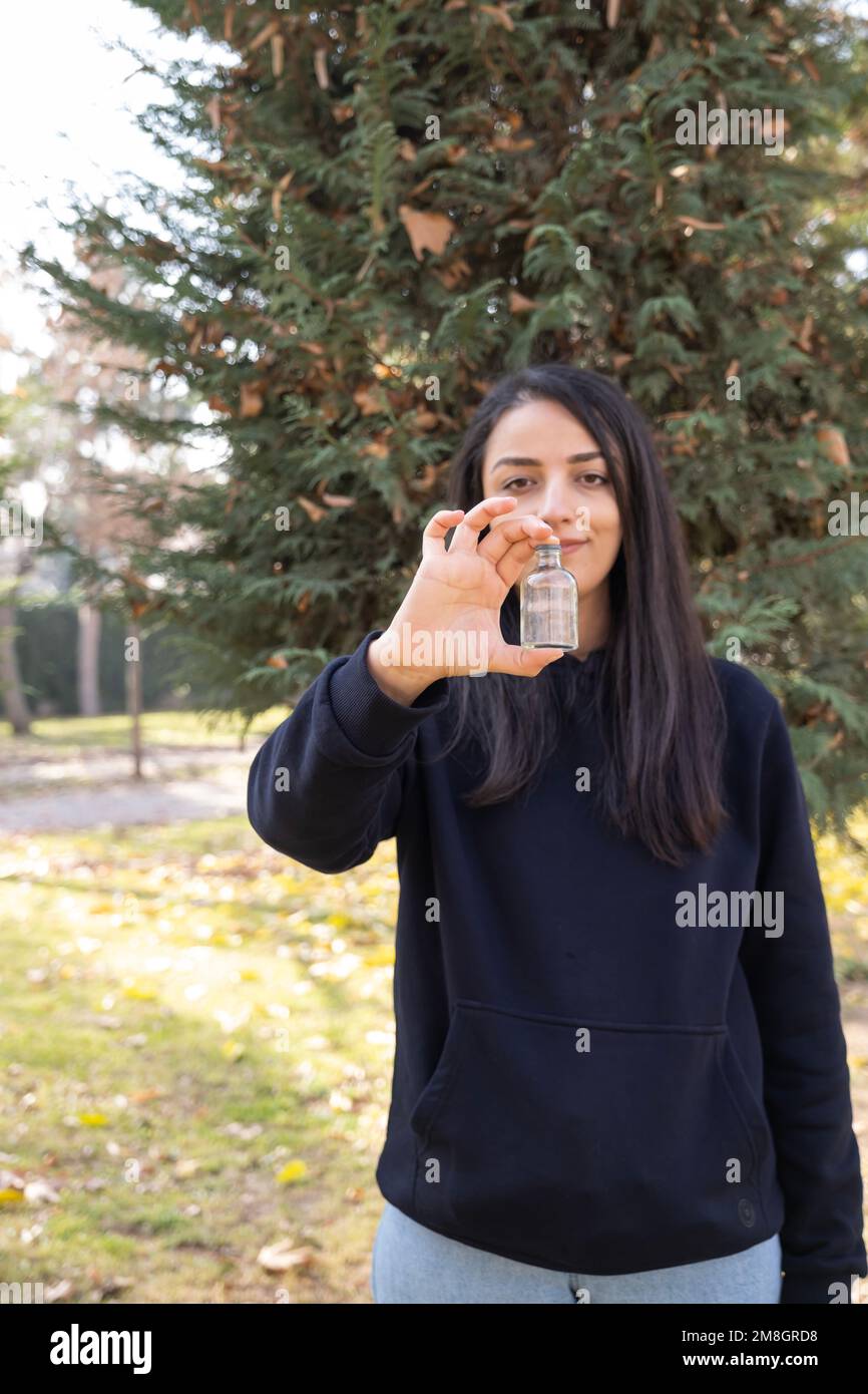 Eine Frau, die eine leere Arzneimittelflasche in der Hand hält. Leeres Label für Modell. Draußen im Park. Gesundheit, Apotheke, Arztkonzept vertikales Bild. Stockfoto